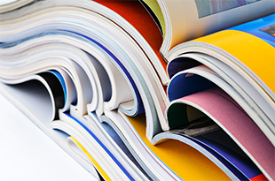 A stack of color journals lie open on a white table.