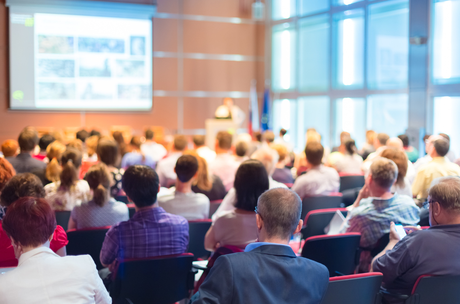 A room full of people watch a presentation.