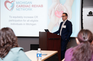 Dr. Mike Thompson presents during the inaugural MiCR Annual Meeting as attendees look on. A slide with the MiCR mission shines from the projector.