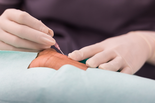 A health care provider wearing gloves and blue scrubs inserts a needle into a patient's wrist.