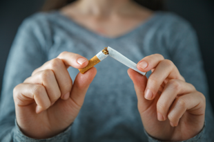 A woman wears a grey, v-neck sweater in this closeup of her hands as she breaks a cigarette in half.