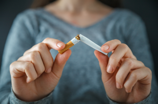 A woman wears a grey, v-neck sweater in this closeup of her hands as she breaks a cigarette in half. 