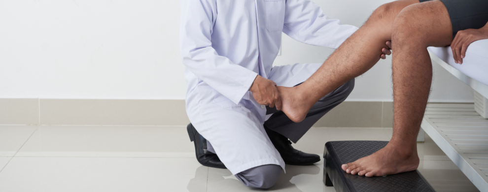 A physician wearing a white coat examines a Black patient's leg.