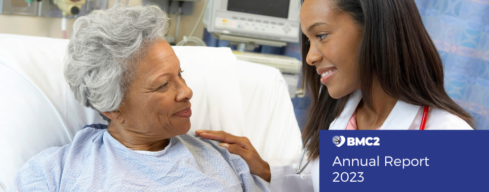 A young Black health care professional talks with an older Black patient.