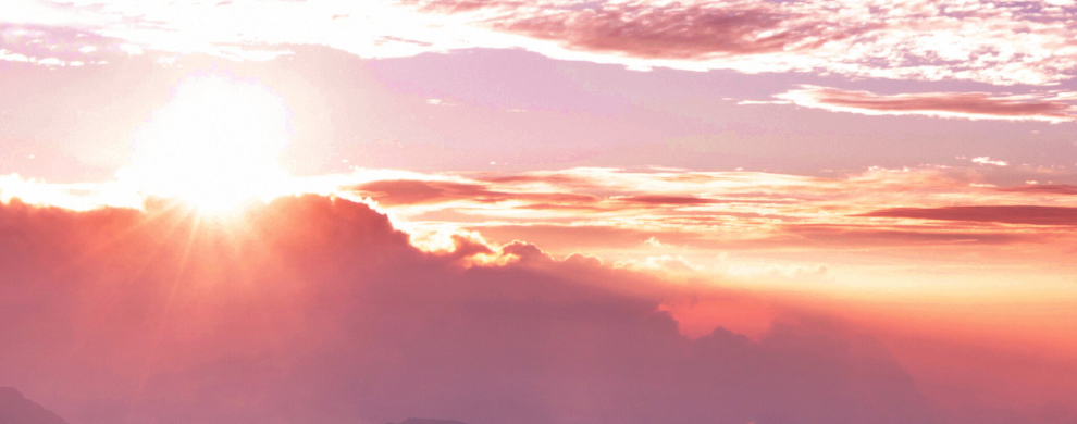 The sun peeks over yellow, pink, and purple clouds.
