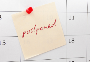 A closeup of a sticky note on a calendar. Handwritten on the note in red, is the word, "postponed."